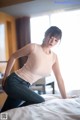 A woman in a pink top and jeans posing on a bed.