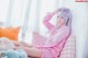 A woman in a pink pajamas sitting on a bed with stuffed animals.