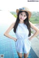 A woman in a blue romper and a straw hat posing by a pool.