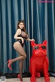 A woman in a black bodysuit and red high heels posing next to a red dog.