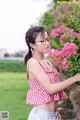 A woman in a red and white checkered top holding a pink flower.