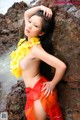 A woman in a red and orange skirt leaning against a rock.