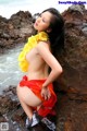 A woman in a red and yellow bikini posing on a rock by the ocean.