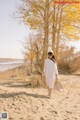 A woman in a white dress and hat walking on a sandy beach.