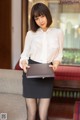 A woman in a white shirt and black skirt holding a laptop.