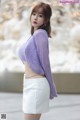 a woman in a purple sweater and white skirt posing for a picture