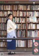 A woman standing in front of a bookshelf holding a book.