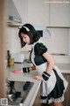 A woman in a maid outfit standing in a kitchen.