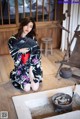 A woman in a kimono sitting on the floor holding a fan.