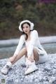 A woman sitting on a rocky beach wearing a white sweater and white boots.