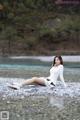 A woman sitting on a rocky beach next to a river.