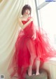 A woman in a red dress sitting on a stool.