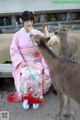 A woman in a pink kimono feeding a deer.