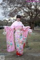 A woman in a pink kimono standing in front of a tree.