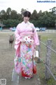 A woman in a pink kimono standing next to a deer.