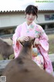 A woman in a pink kimono petting a deer.