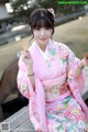 A woman in a pink kimono sitting on a wooden bench.