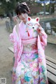 A woman in a pink kimono holding a white cat mask.