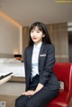 A woman in a business suit sitting on a red chair.