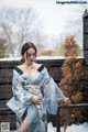 A woman in a blue kimono standing on a balcony in the snow.