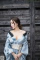 A woman in a blue kimono standing in front of a wooden wall.