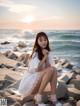 A woman sitting on a rock by the ocean at sunset.