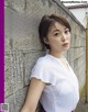 A woman leaning against a wall in a white shirt.