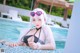 A woman in a bikini and sunglasses sitting by a pool.