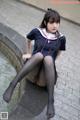 A woman in a school uniform sitting on a fountain.