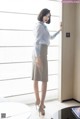 A woman in a white shirt and gray skirt leaning against a wall.