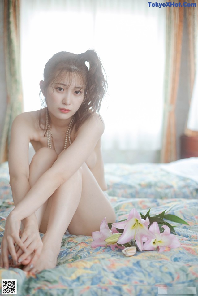 A naked woman sitting on a bed with flowers.