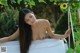 A naked asian woman sitting on a white bench in a garden.