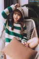 A woman sitting in a wicker chair wearing a green and white striped sweater.