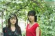 Two young women standing next to each other in front of trees.