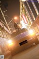 A woman sitting on top of a car in the middle of a city.