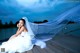 A woman in a wedding dress sitting on a dock.